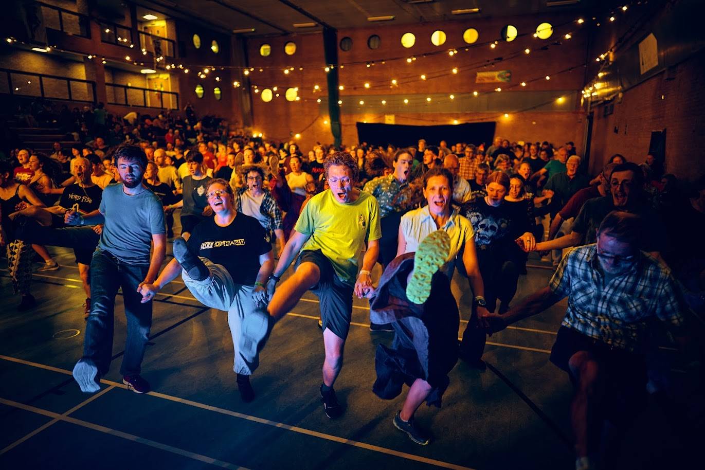 Lines of happy dancers kicking high as they dance the Cornish Six Hand Reel